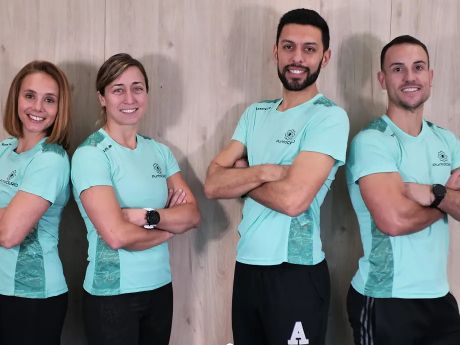 Cuatro entrenadores de Punto Cero, con las camisetas de la casa, de brazos cruzados delante de la pared de madera de la sala