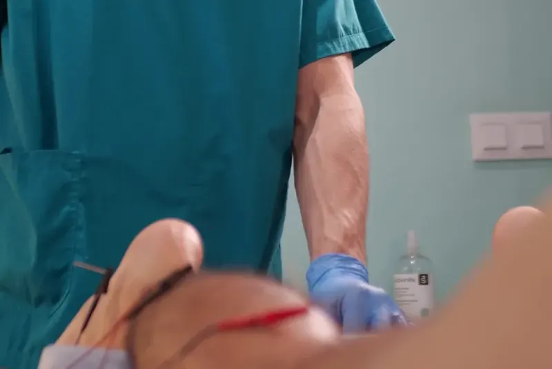 Las manos con guantes de un fisioterapeuta sobre la rodilla de un paciente, con el cable rojo de la técnica