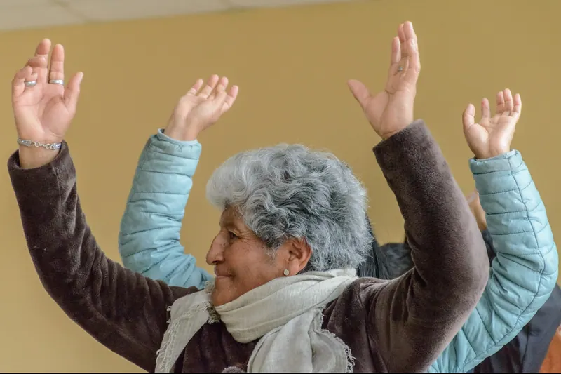 Una señora mayor levanta los brazos en una clase de ejercicio en grupo